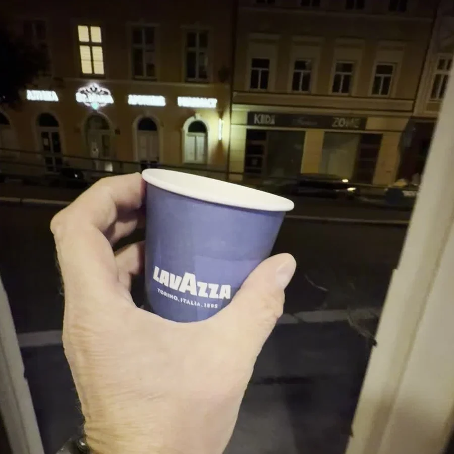 Kelímek Lavazza s čerstvou kávou ve dveřích prodejny, noční Zámecký vrch