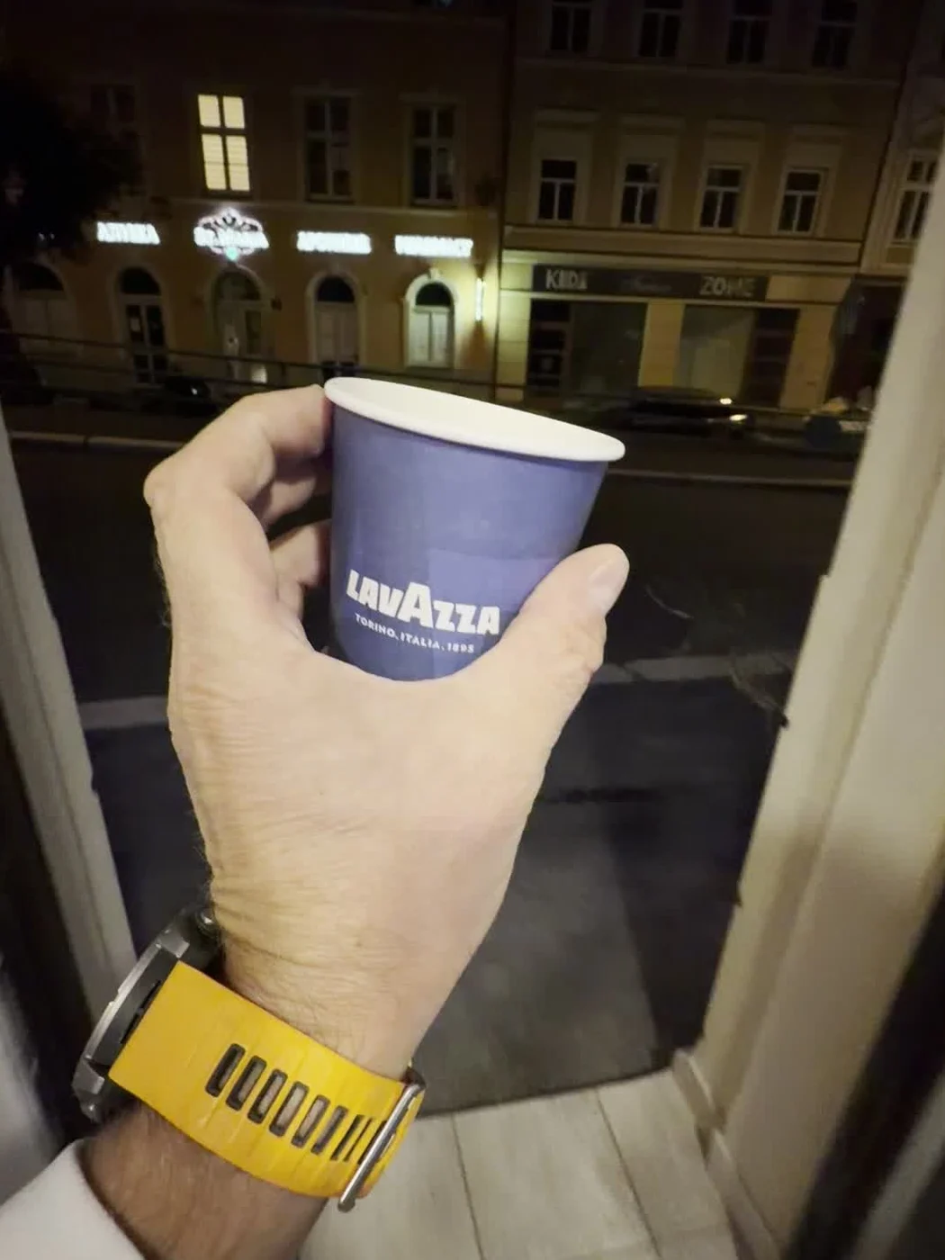 Kelímek Lavazza s čerstvou kávou ve dveřích prodejny, noční Zámecký vrch